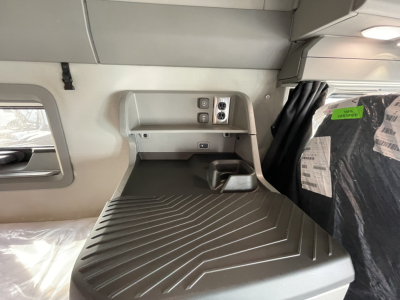 Interior of a new Volvo VNL64T860 sleeper cab showing a raised shelf with electrical outlets and a molded rubber cargo bed. Visible text on sticker/labeling near window and seat area.