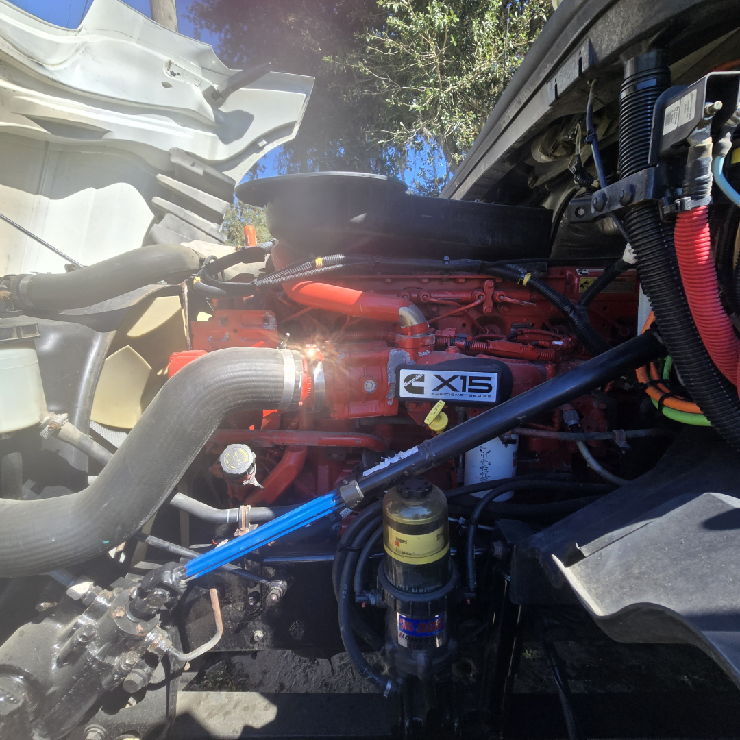 Truck engine bay showing Cummins X15 engine label and surrounding hoses and components in a daycab cab interior view.