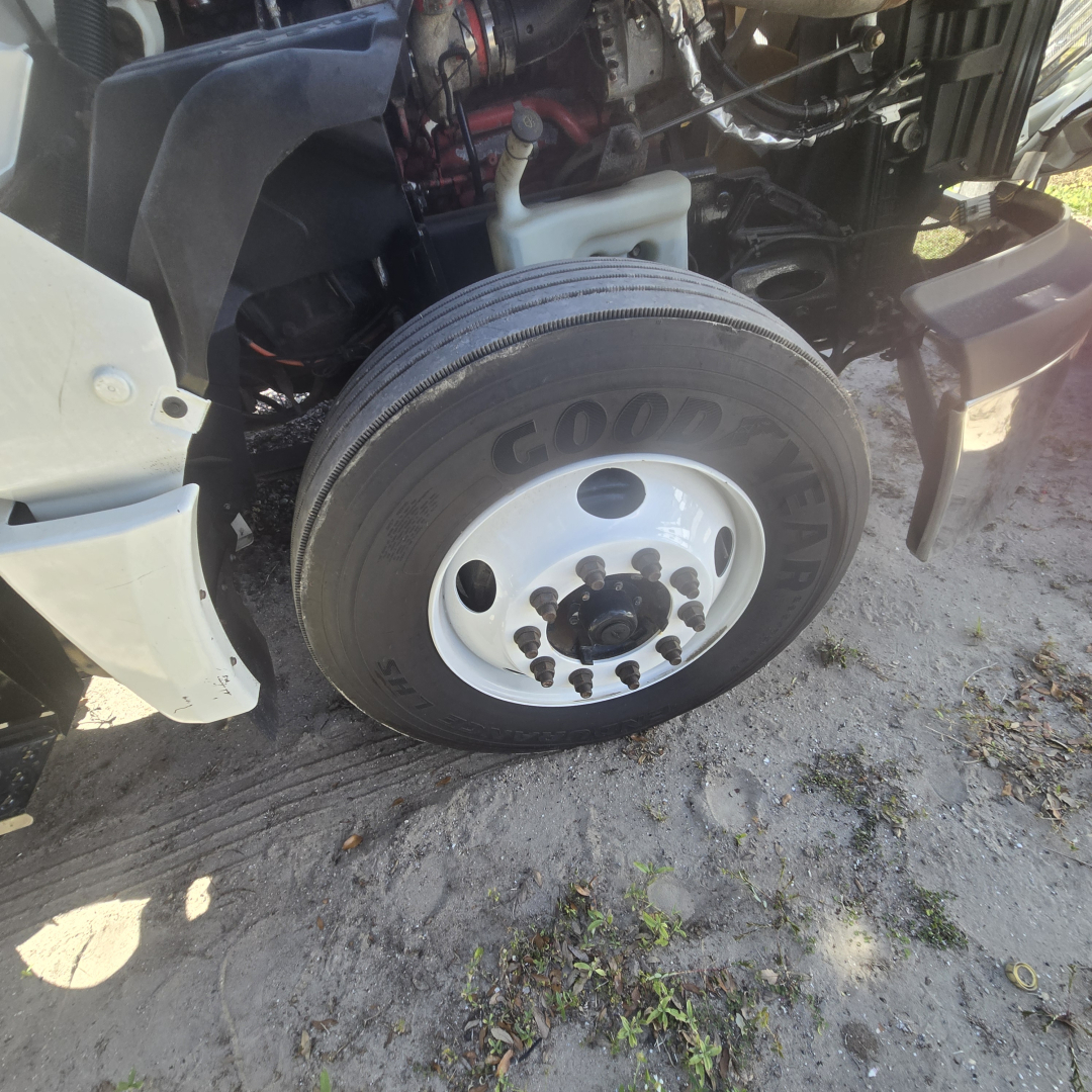 Wheel and front-left hub area of a 2018 International LT625 conventional truck showing Goodyear tire and white steel wheel, partial engine bay and coolant reservoir visible.