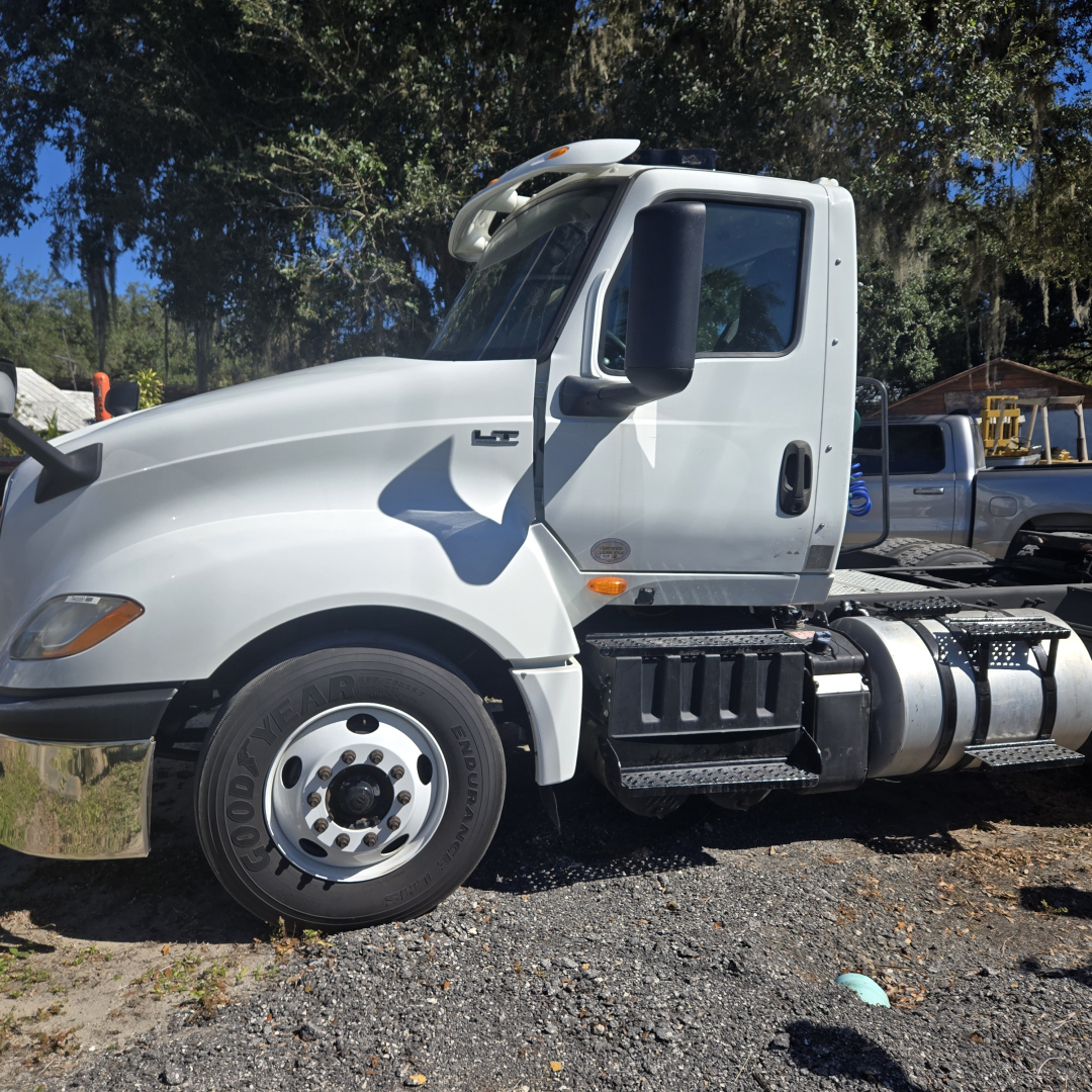 Truck cab side view of a white 2018 International LT625 conventional with HC badge, showing front wheel, door, and fuel tanks.