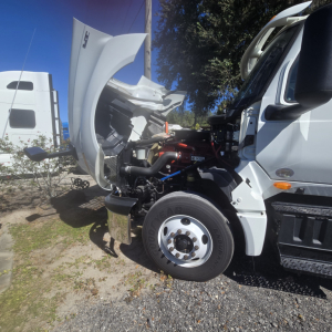 Truck engine bay view of a 2018 International LT625 Conventional with hood raised, showing front wheel, engine components, hoses, and radiator area.