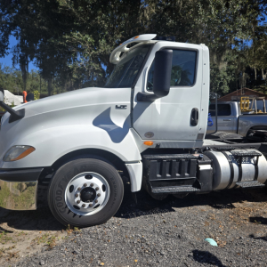 Truck cab side view of a white 2018 International LT625 conventional with HC badge, showing front wheel, door, and fuel tanks.