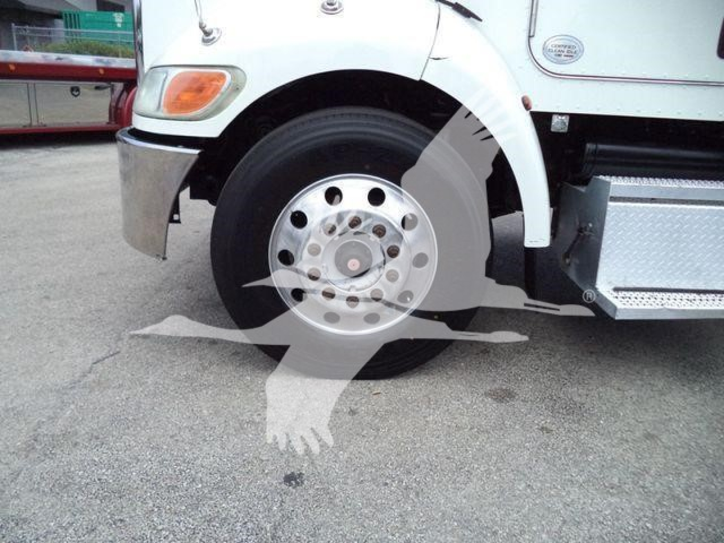 Front left wheel and fender of a white Peterbilt 337 reveals wheel hub, tire, chrome bumper, side step, and a Campagnolo style logo overlay? visible text not legible.
