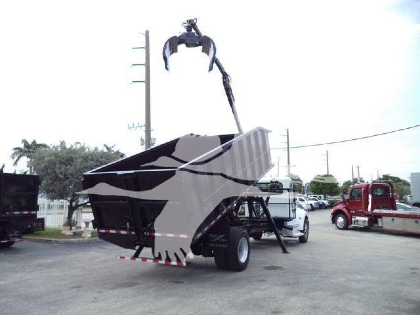 Peterbilt 337 grapple truck with hydraulic material handler in a truck yard; rear hopper elevated; crane/grapple arm visible