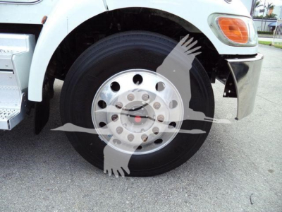 Front wheel and fender area of a 2020 Peterbilt 337 truck showing a steel rim with multiple lug holes and a hub cap, partial front bumper, and headlight.