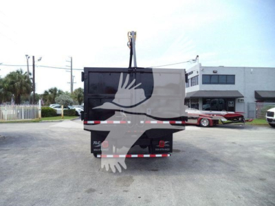 Peterbilt 337 grapple truck rear view with hanging crane hook, tailgate, and dealership building in background.