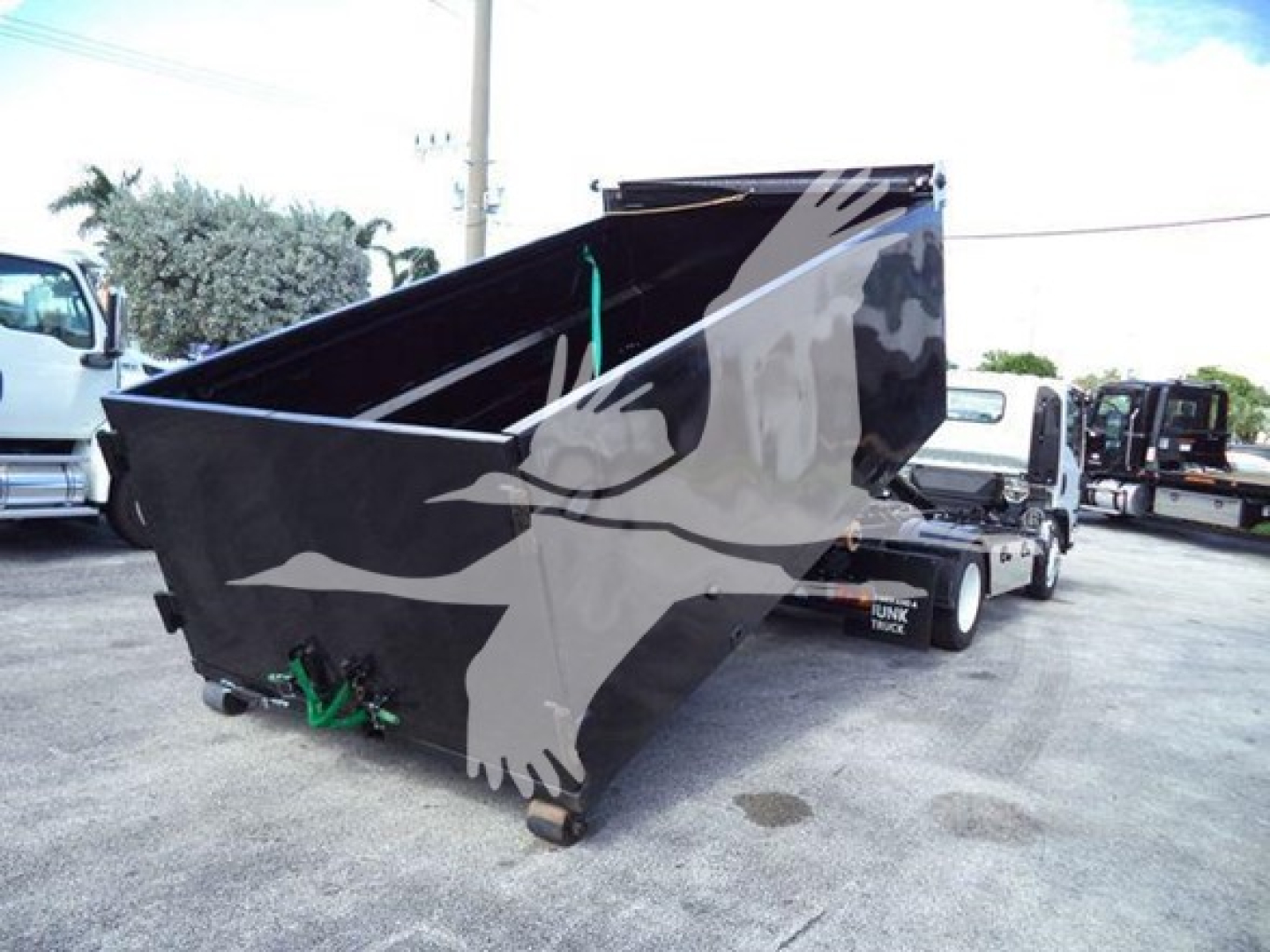 Isuzu NPR HD truck with a large black hooklift bed in a yard.