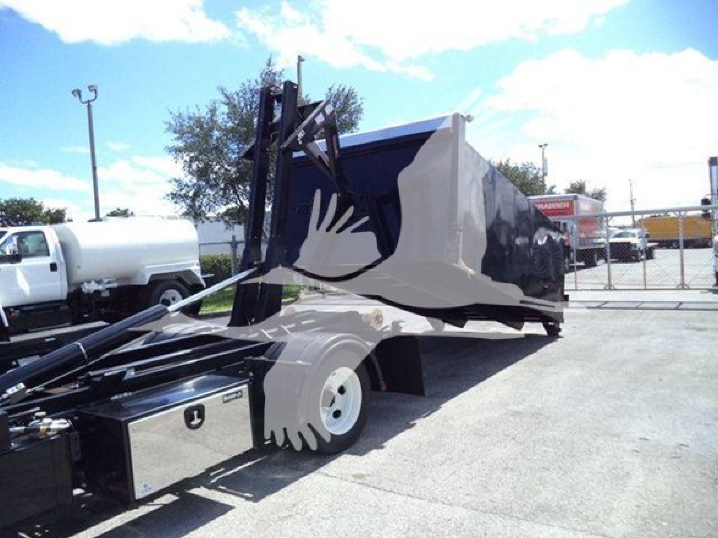 Isuzu NPR-HD truck with a large hooklift bed and hydraulic lifting arm in a disposal or handling setting.