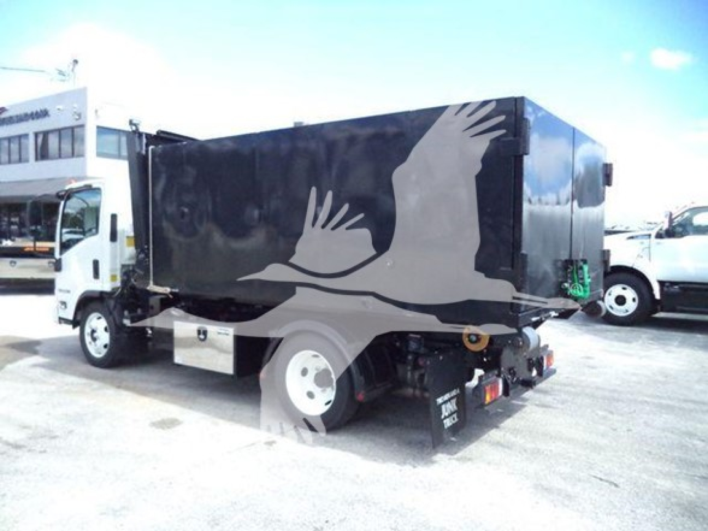 Isuzu NPR HD hooklift truck equipped with a black cargo body featuring a white crane or bird graphic on the side.