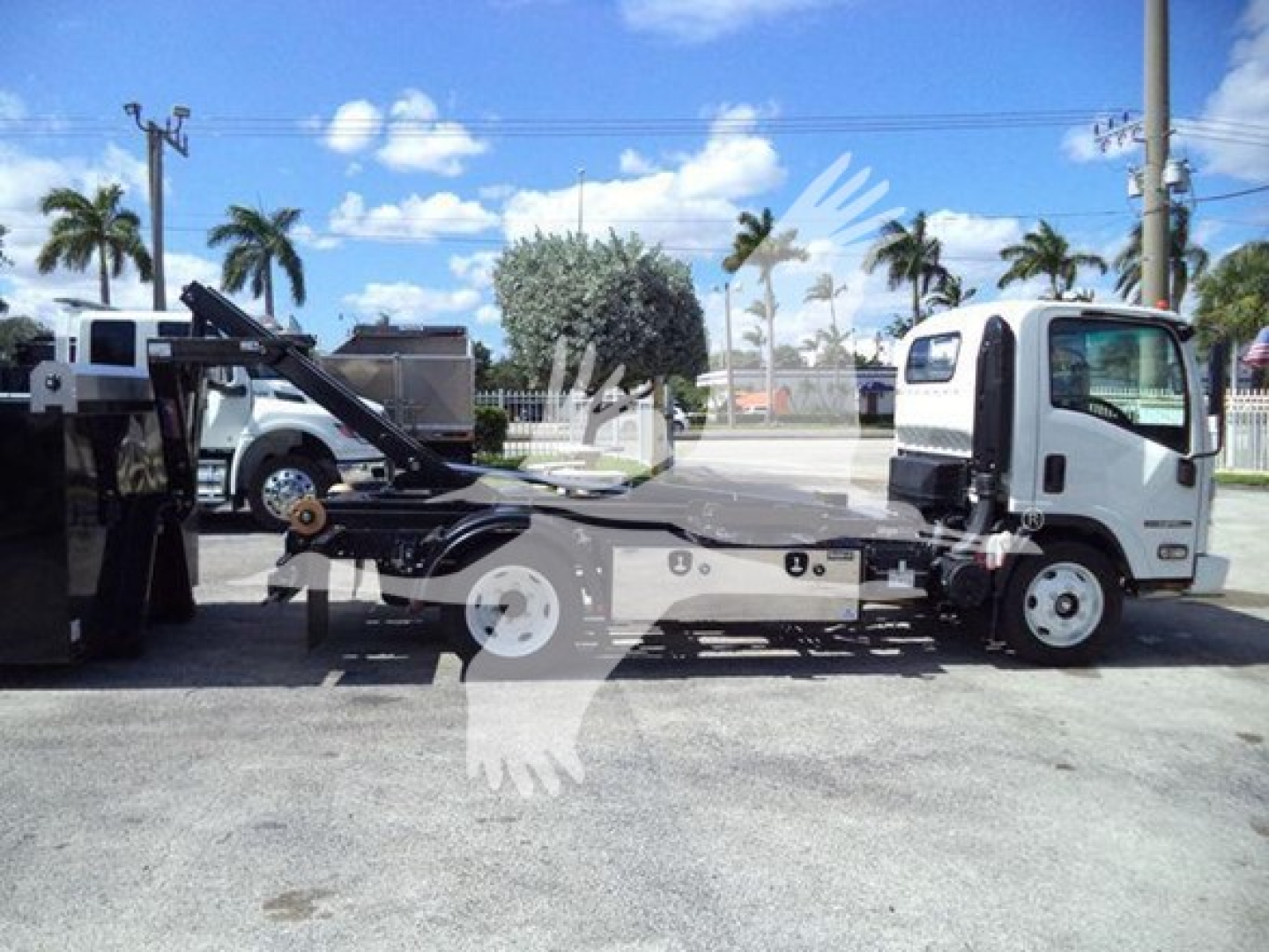 Isuzu NPR-HD hooklift truck side view showing cab and flatbed with hydraulic hooklift, white cab, light background.