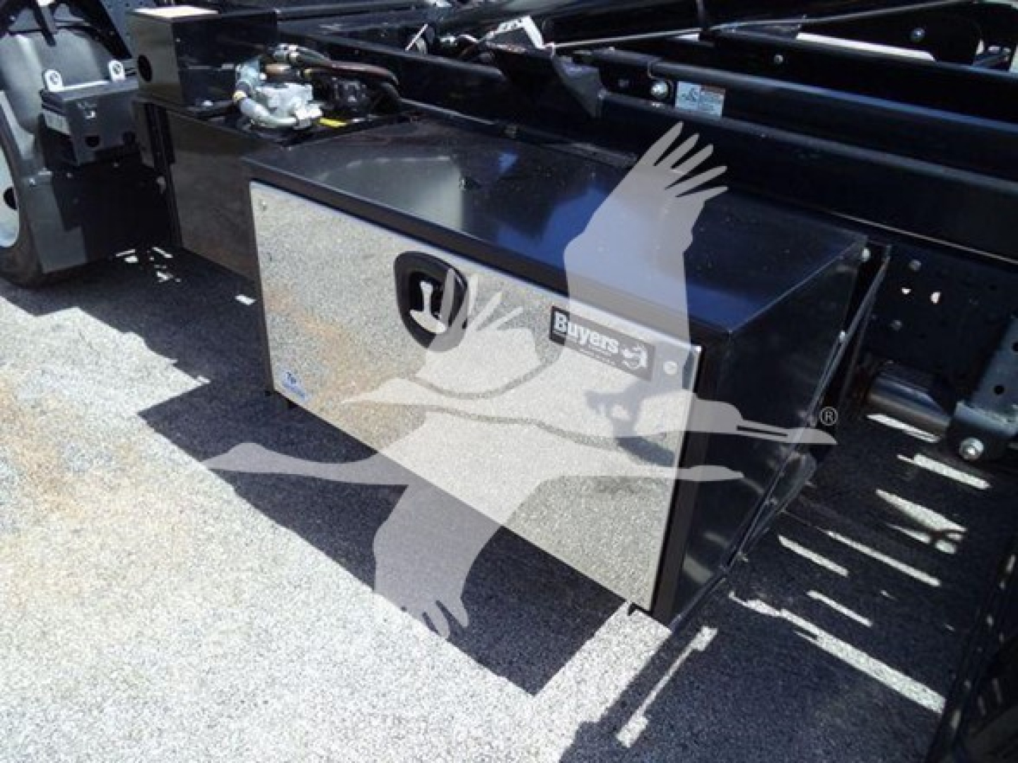 Isuzu NPR-HD truck chassis showing a metal toolbox with Honda? logo and isuzu emblem, mounted on frame with hydraulic components nearby.
