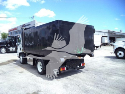 Isuzu NPR HD box truck in a parking lot with black cargo box and white cab seen from rear-left; rear bumper, taillights, and mud flaps visible.