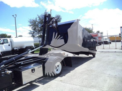 Isuzu NPR-HD truck with a large hooklift bed and hydraulic lifting arm in a disposal or handling setting.