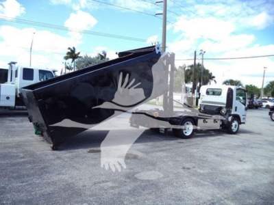 Isuzu NPR-HD hooklift truck with a raised dump bed in a dealership lot. Side view shows cab and chassis with hoist mechanism, other trucks in background.