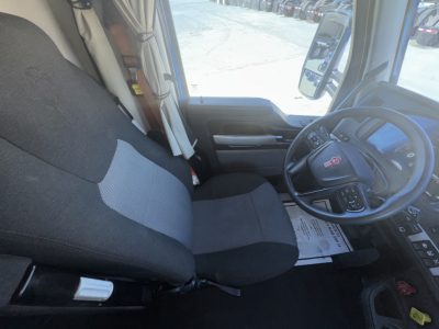 Cab interior of a 2023 Kenworth T680 showing driver seat and steering wheel with dashboard and door panel.