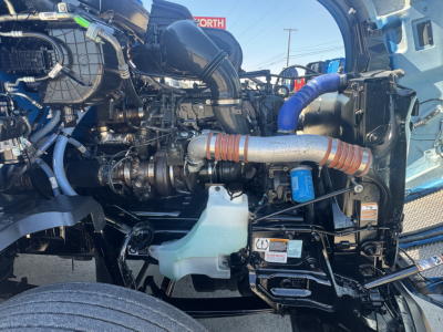 Kenworth T680 engine bay showing coolant reservoir, blue hoses, and turbo piping.