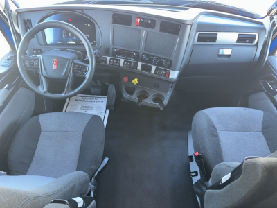Kenworth T680 interior dashboard and seating from driver and passenger seat view showing steering wheel, instrument cluster, center console, and cup holders.