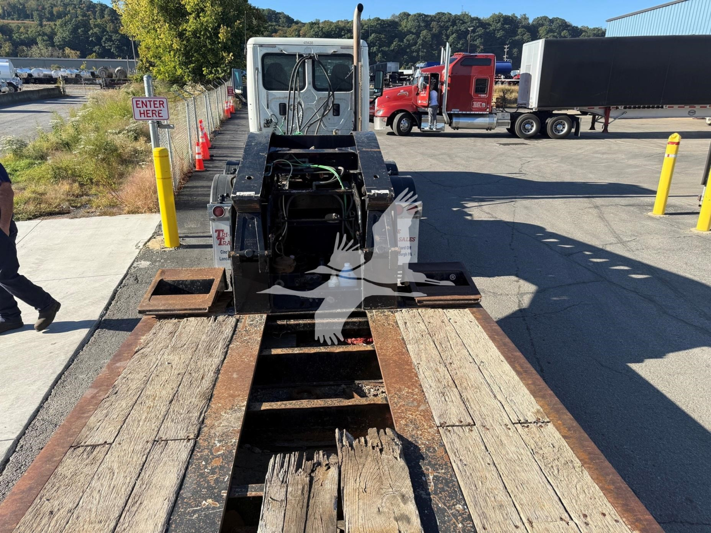Towable lowboy trailer with Tk110Hdg unit, view from rear showing deck and gooseneck connection. Weathered wooden deck planks and steel framework visible.