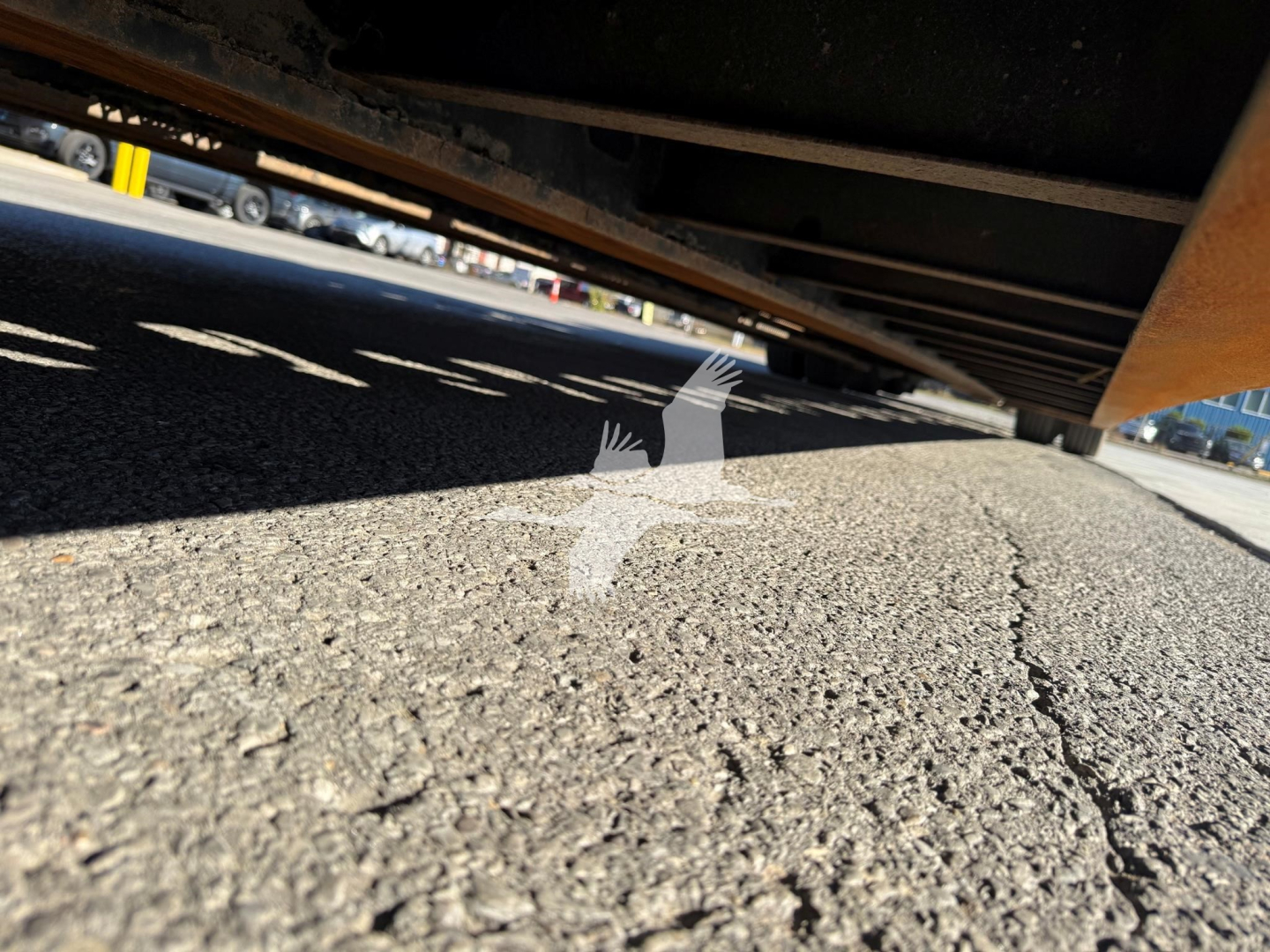 Underbelly view of a Trail King TK110HDG trailer showing the underside and ground texture.