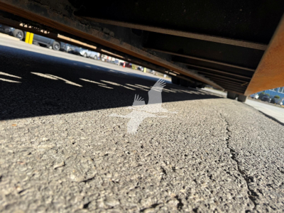 Underbelly view of a Trail King TK110HDG trailer showing the underside and ground texture.