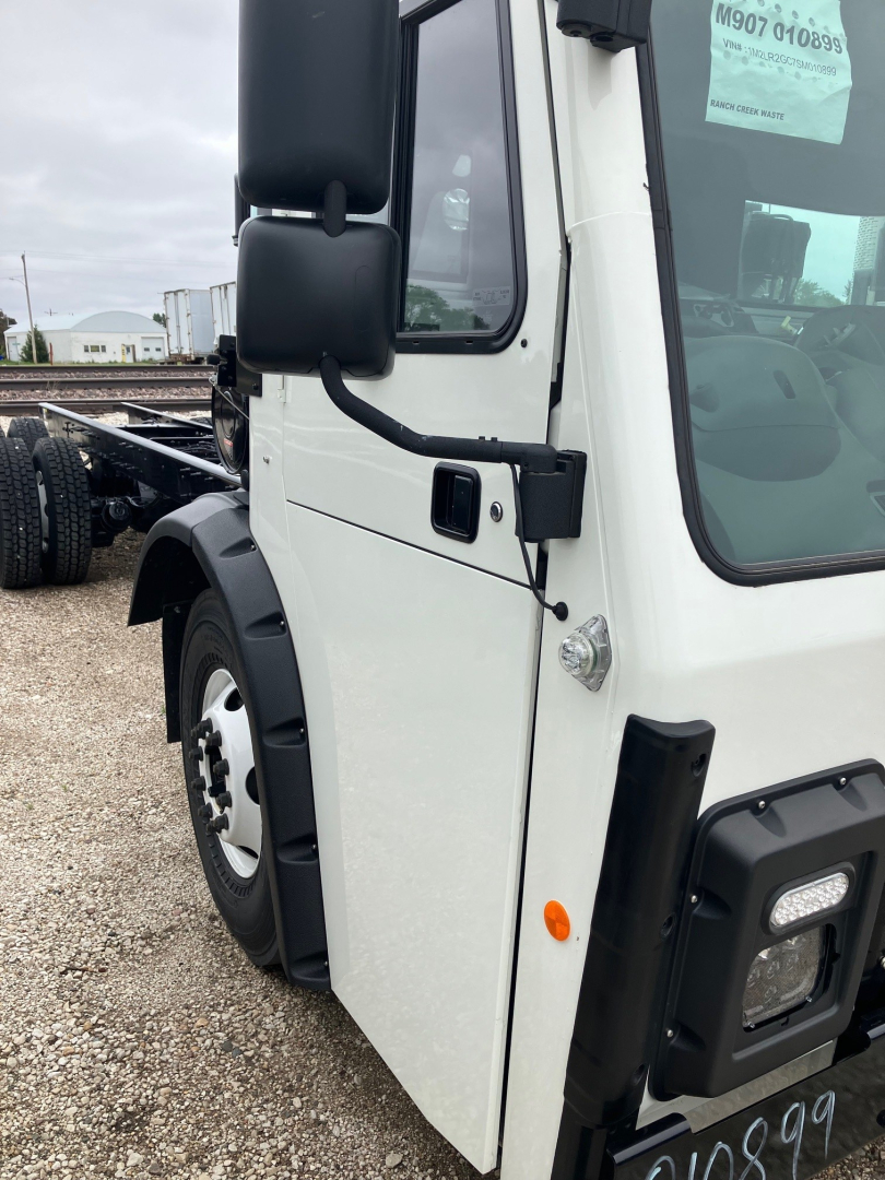 Truck cab close-up showing white exterior, black mirrors, and door area of a Mack LR64 chassis cab.