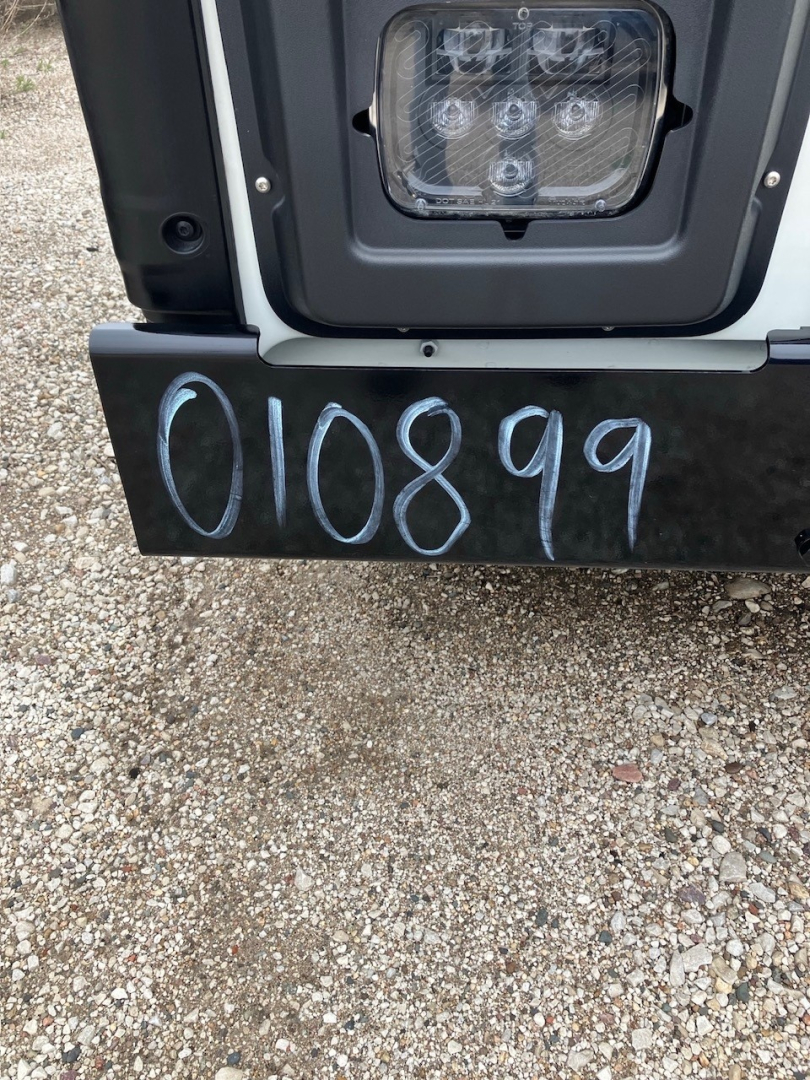 Front bumper area of a 2025 Mack LR64 cab and chassis showing the rear tail/step area with the stock number 010899 written on the bumper and a light housing.