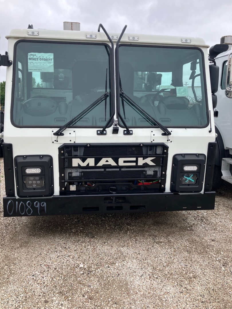 Mack LR64 cab and chassis front showing large grille with 'MACK' badge, dual windshield wipers, and white cab; VIN sticker on left window and stock number on windshield.