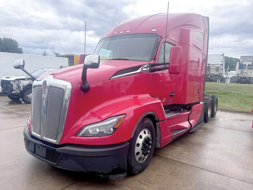 Kenworth T-680 Next Gen red semi-truck in a parking lot, front three-quarter view showing cab, grille, headlights, and side mirror.