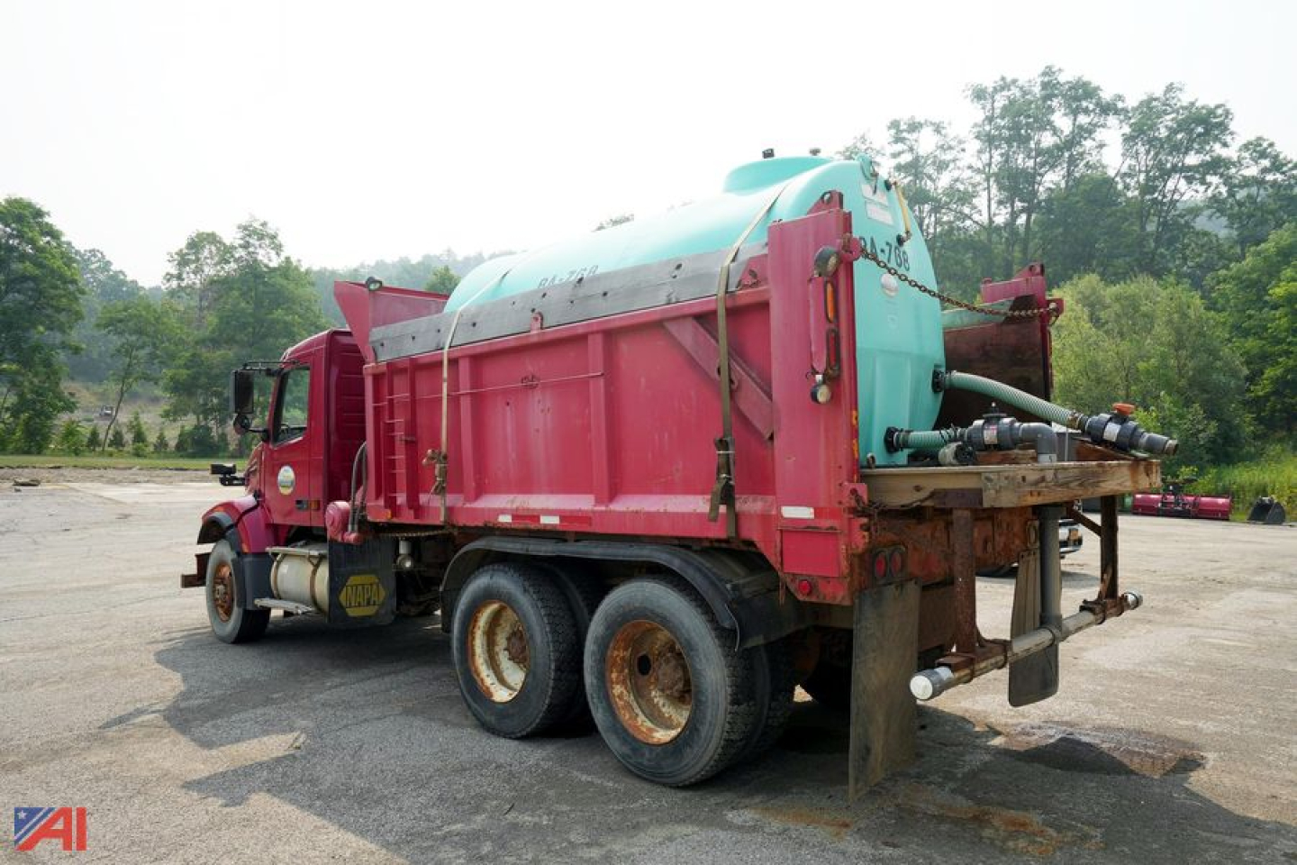 Dump truck back view showing large turquoise tank and red chassis with hoses and hitch.