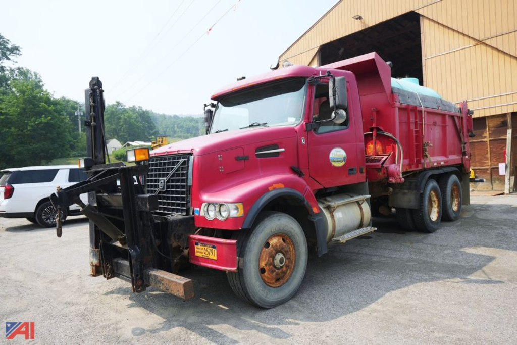 Dump truck with red cab and dump bed showing front bumper, wheel arches, and hydraulic lift in a yard.