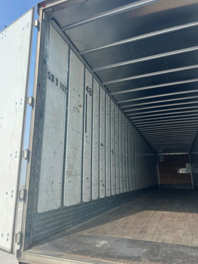Interior of a freight trailer showing metal side walls with numbers and wooden floor.