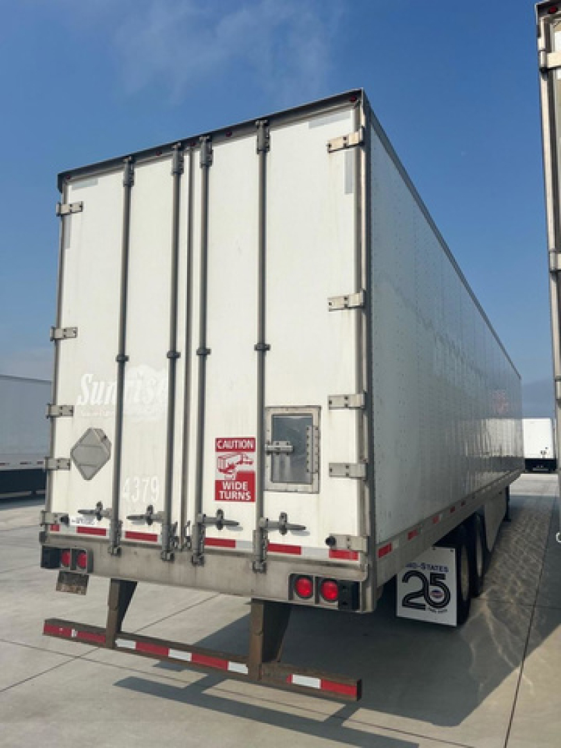 Rear of a white utility trailer with double doors, CAUTION label, lock latches, and tail lights visible. Side shows 'Sun' branding faintly; undercarriage shows bumper and license plate area.