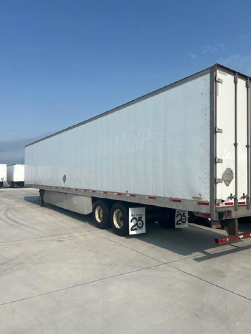 Trailer side view showing a long light-gray refrigerated or dry van trailer attached to landing gear with tandem axles and rear doors.