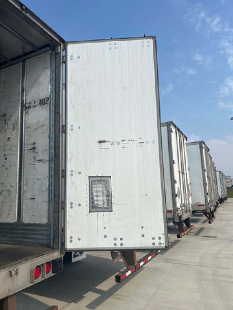 Utility van trailer side door with metal exterior panels and vent; row of trailers parked along a lot.