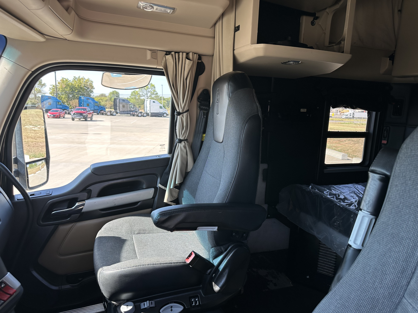 Truck cab interior with driver's seat, steering area, and ceiling storage. Visible text on panels not legible.
