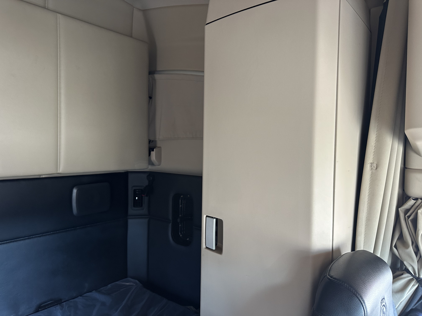 Truck cab interior showing sleeper area with cream upholstery and partition; door area and IT panel visible in a Kenworth T680 cab