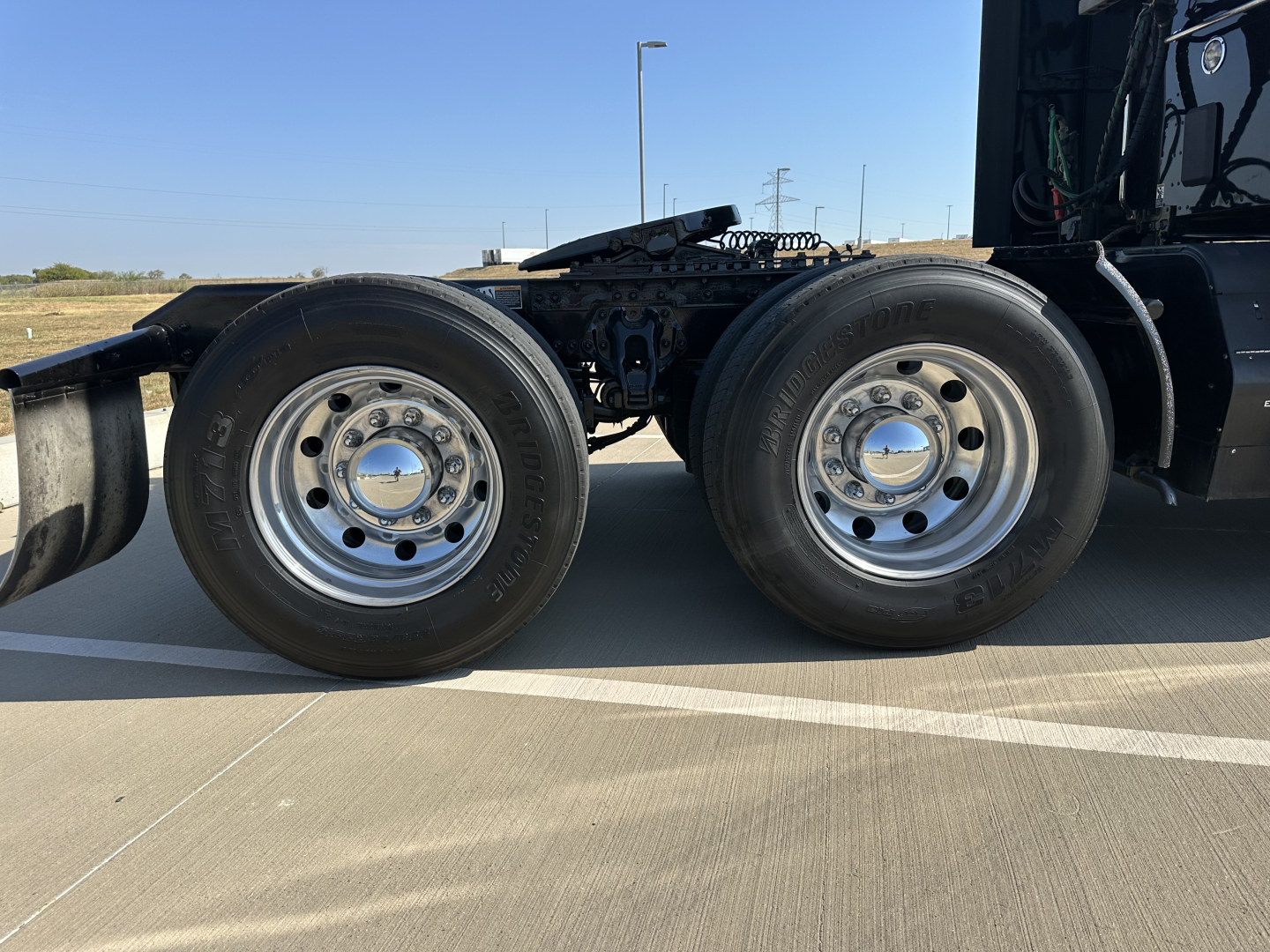 Dual rear wheels of a Kenworth truck showing polished rims and tires, part of the chassis and air lines visible