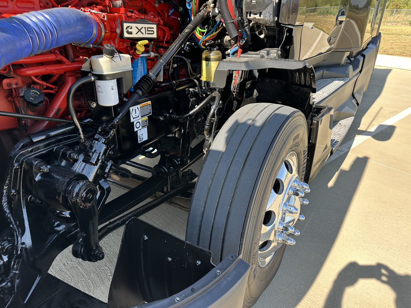 Kenworth T680 front suspension and wheel well with exposed engine components and blue intake hose visible.