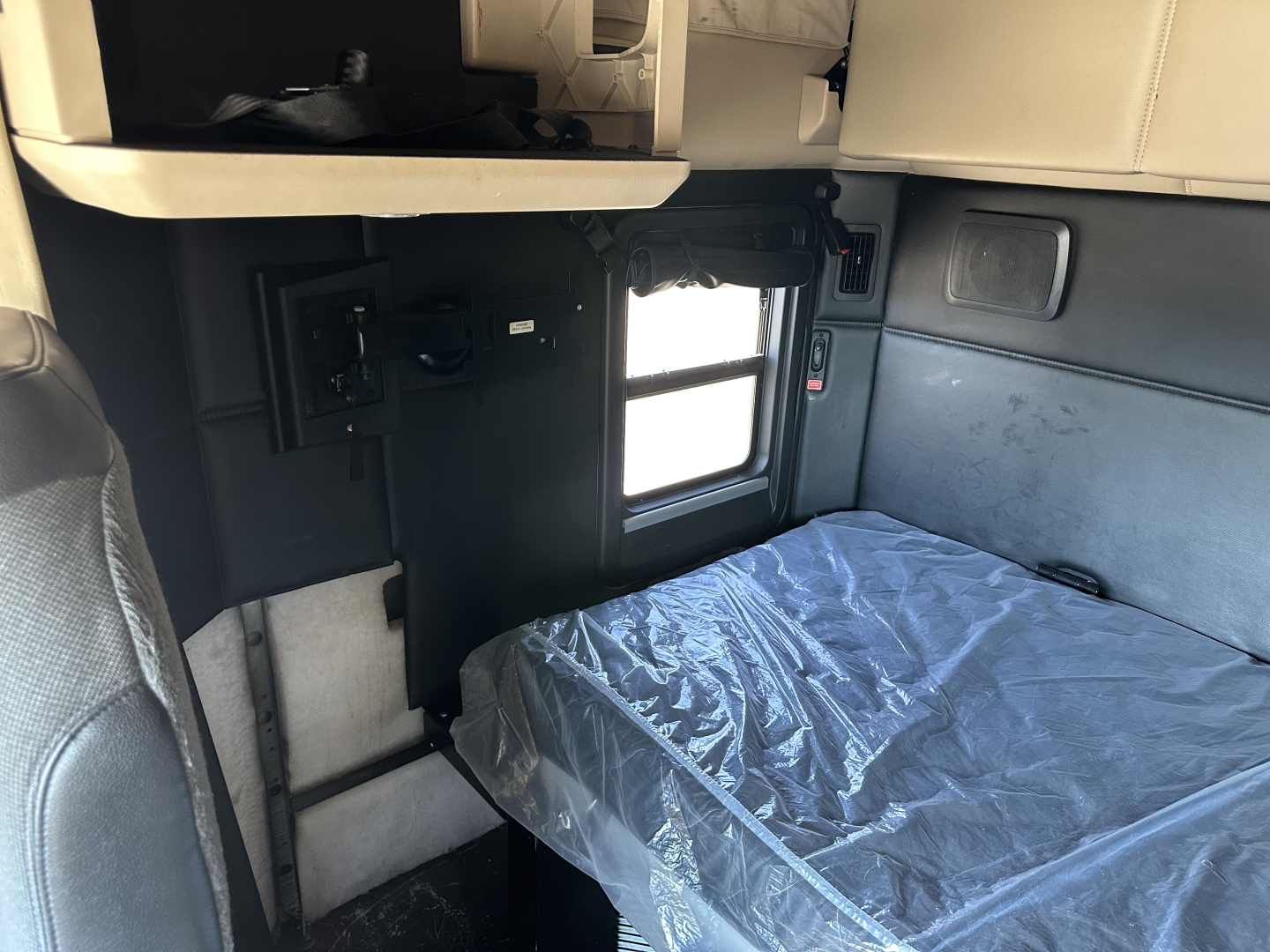 Kenworth T680 sleeper cab interior showing a bed with plastic covering and side window, with storage compartments and controls visible.