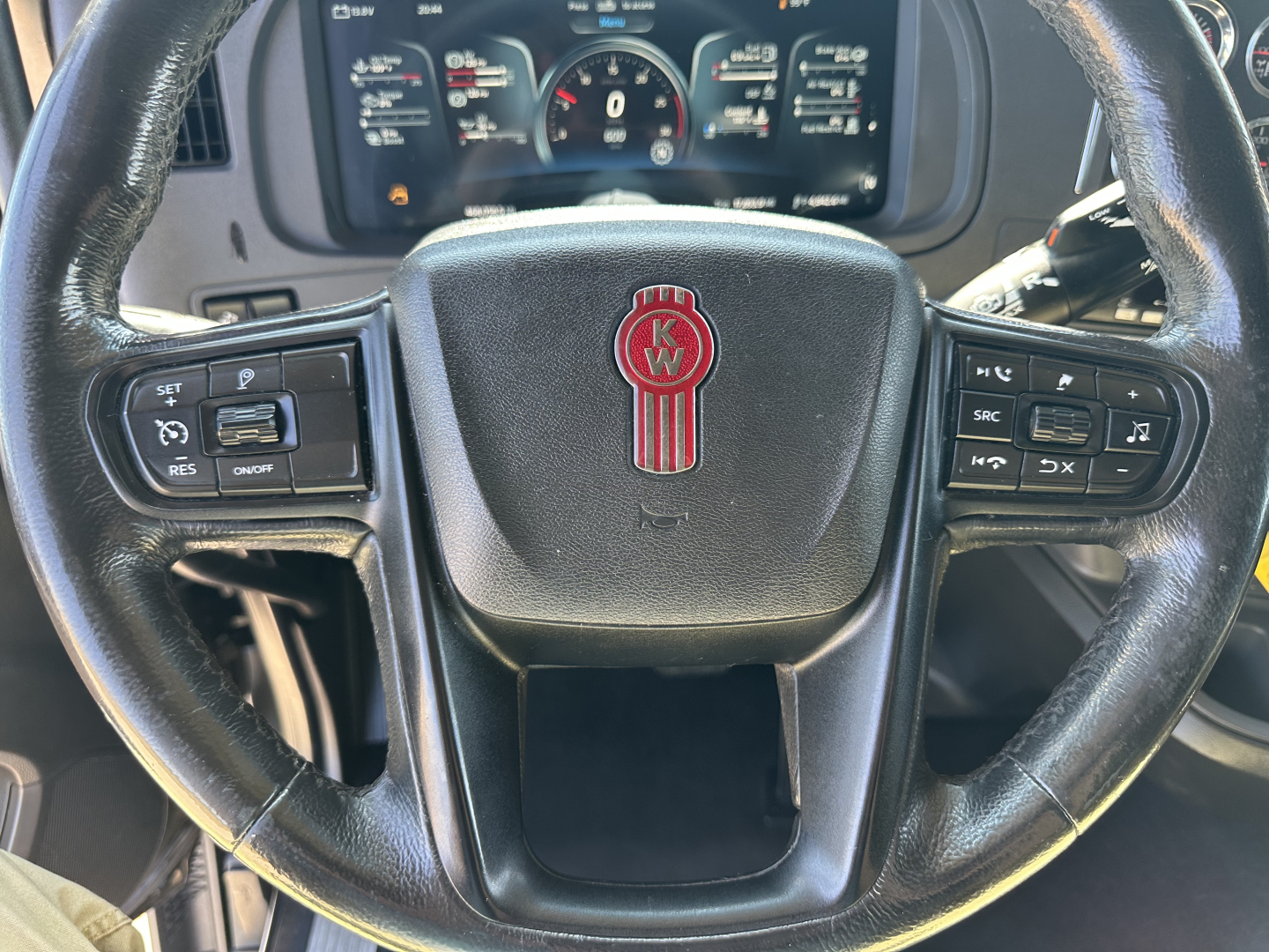 Kenworth T680 steering wheel with KW emblem and dashboard controls visible; looks like a truck interior shot.