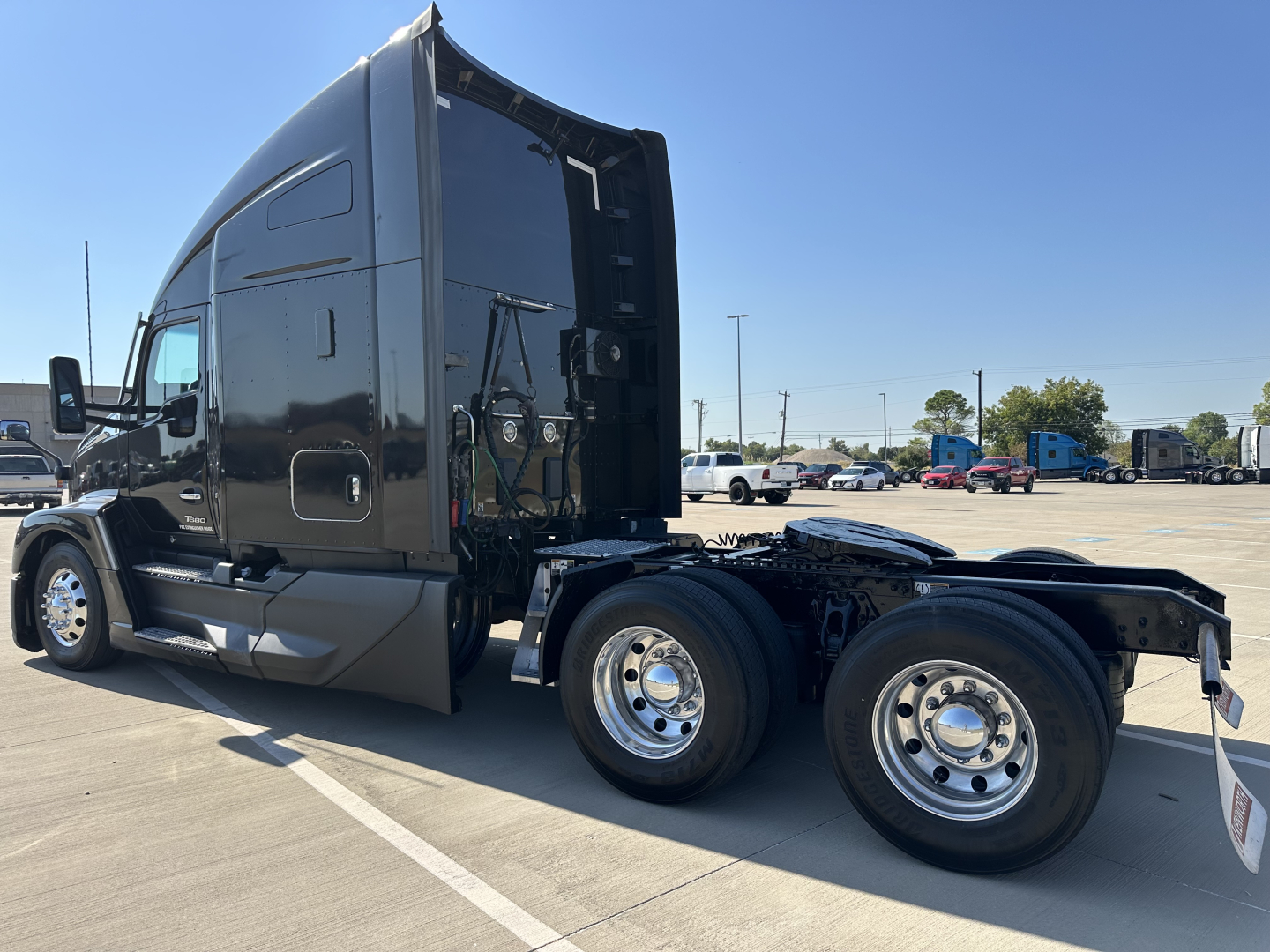 Kenworth T680 tractor in black, side view showing cab and rear dual wheels without trailer, with visible background trucks in a lot.