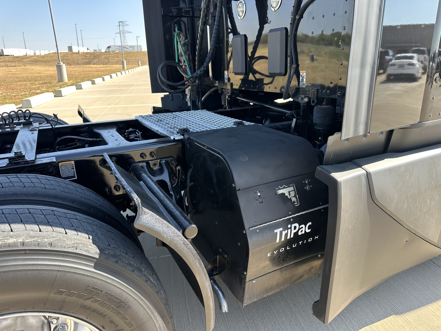 Kenworth T680 tractor cab area showing black TriPac Evolution auxiliary power unit housing and chassis components.