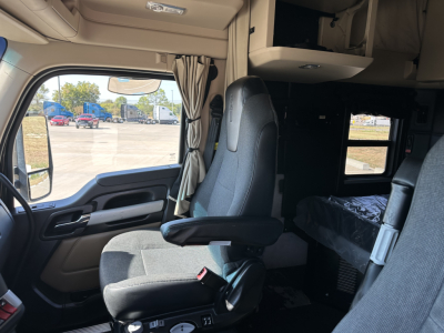 Truck cab interior with driver's seat, steering area, and ceiling storage. Visible text on panels not legible.