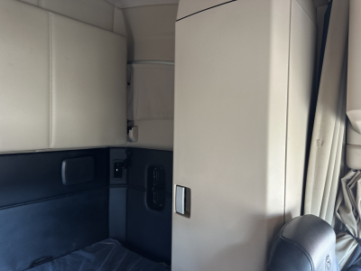 Truck cab interior showing sleeper area with cream upholstery and partition; door area and IT panel visible in a Kenworth T680 cab