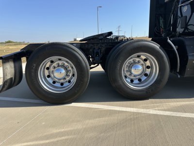 Dual rear wheels of a Kenworth truck showing polished rims and tires, part of the chassis and air lines visible