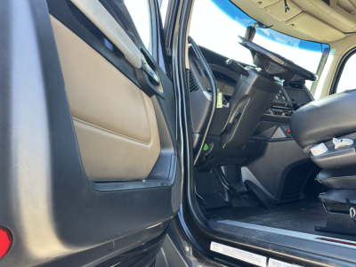 Truck interior door sill and driver area of a 2022 Kenworth T680 showing the cabin floor, seat, steering wheel, and dashboard.