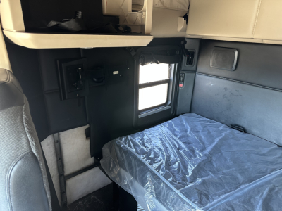 Kenworth T680 sleeper cab interior showing a bed with plastic covering and side window, with storage compartments and controls visible.