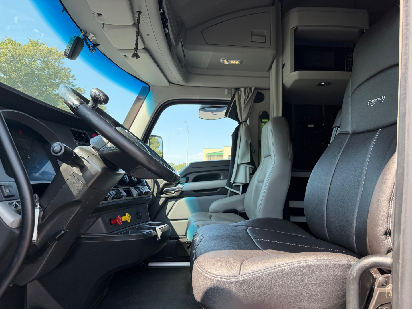 Kenworth T680 truck interior cab view showing driver seat and dashboard with steering wheel and overhead storage.