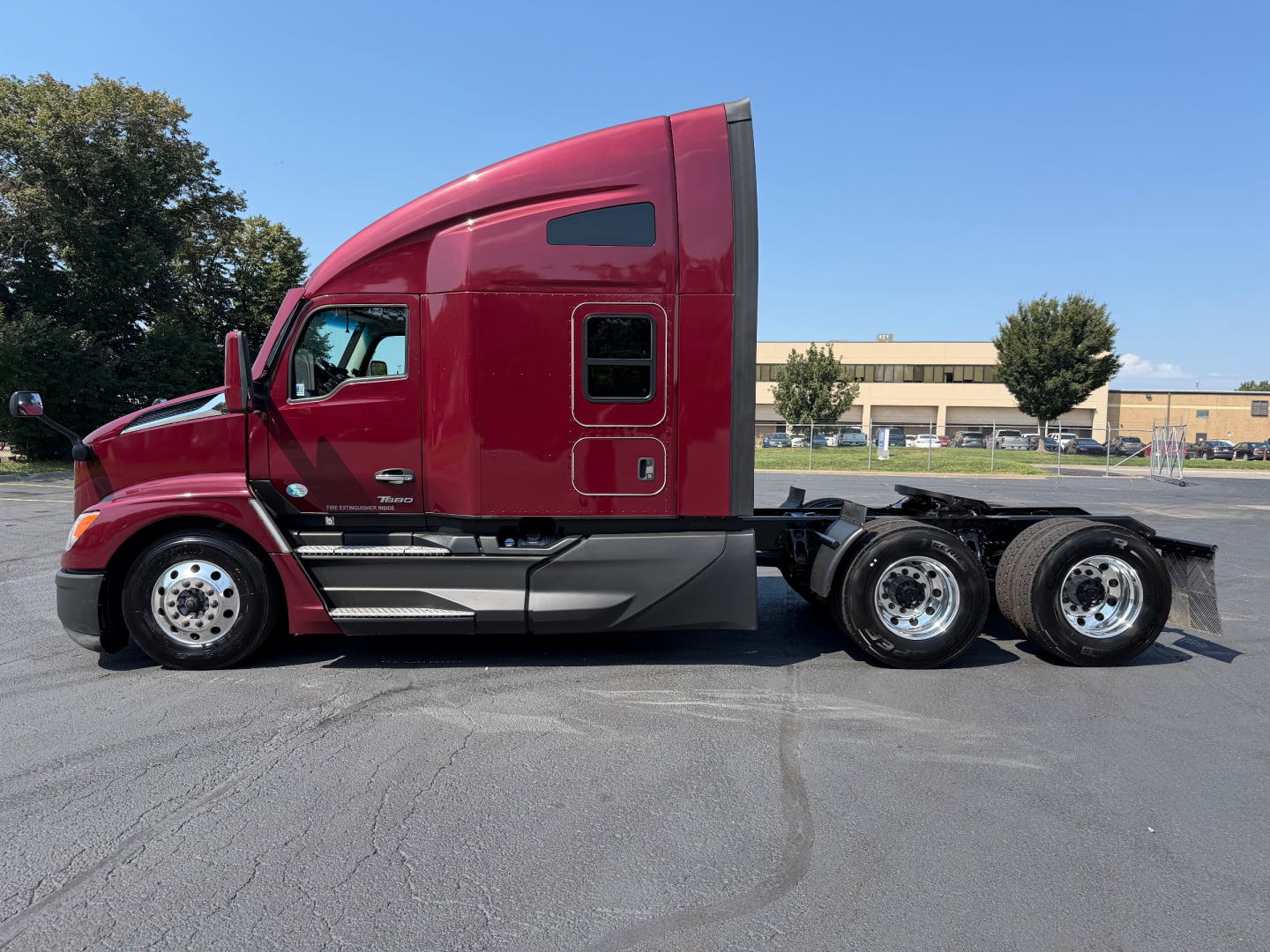 Kenworth T680 tractor side view showing red cab and rear wheels, with no visible text on components.
