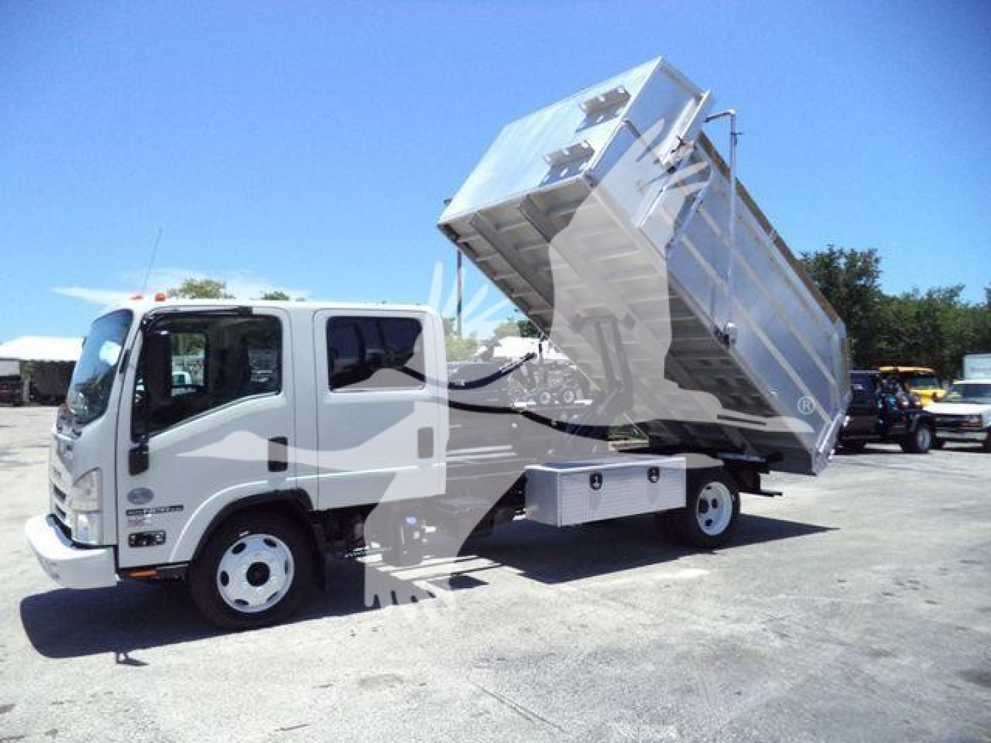 Isuzu NPR-HD dump truck with raised aluminum dump body in a truck yard.